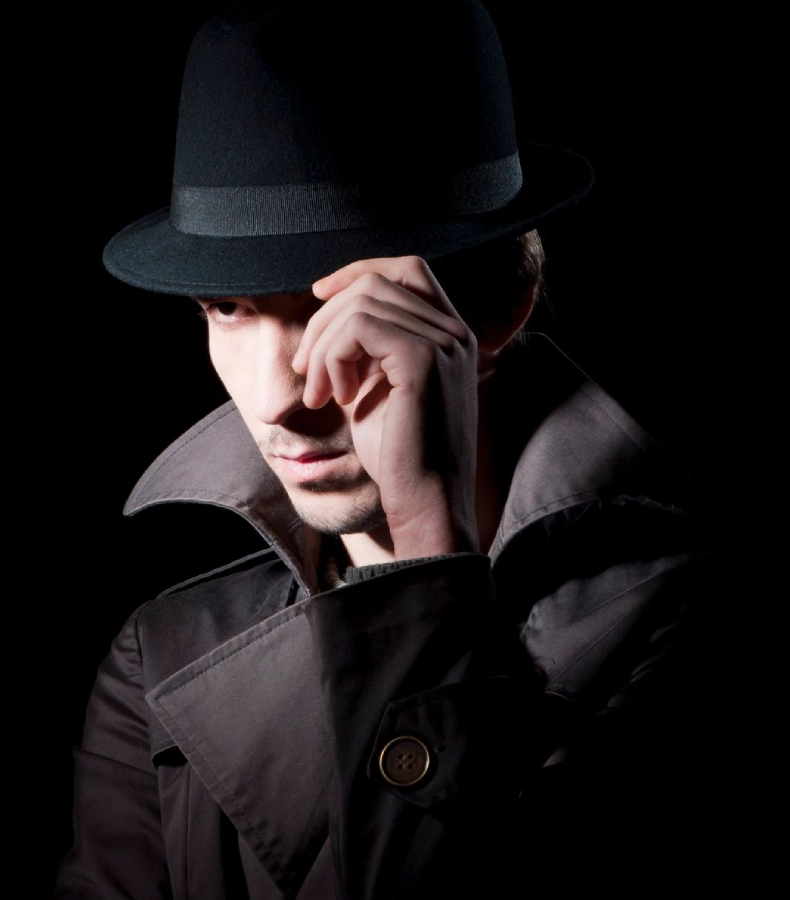 A man in a hat and jacket holding his hand to the side of his face.