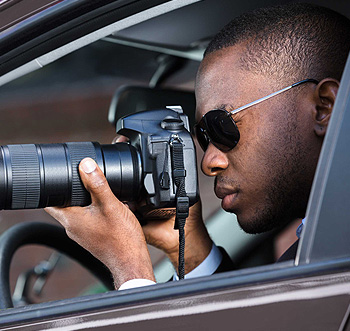 Licensed private investigator conducting vehicle surveillance with a camera